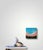 This mixed media piece captures a serene beach scene, where vibrant turquoise waters meet a soft, coral-hued shore. The...