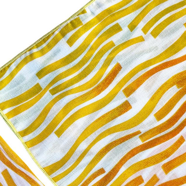 A set of four square fabric dinner napkins with orange and yellow design. Dimensions: 17" x 17"