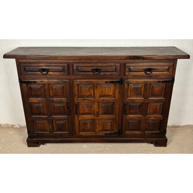 Attractive Spanish hardwood sideboard featuring a classic paneled door design and three upper drawers, enhanced with...