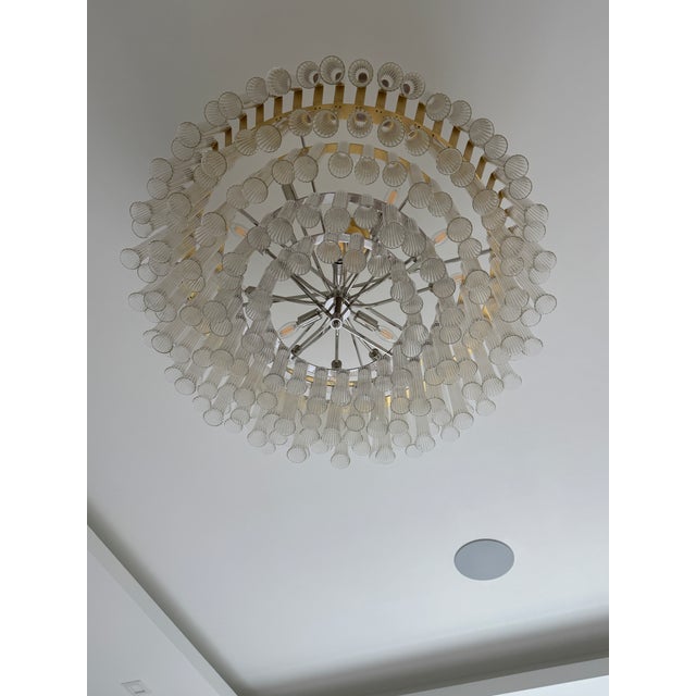 The Lorelei by Julie Neill showcases elegant, fluted glass tubes thoughtfully arranged in cascading, concentric circles...