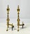 A striking pair of polished brass fireplace andirons featuring traditional urn finials above a bold spiral-twist (flame-...