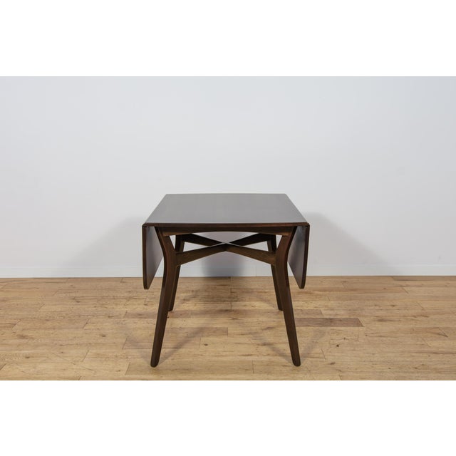 The table is equipped with a distinctive butterfly-leaf mechanism featuring two drop leaves, allowing it to function both...