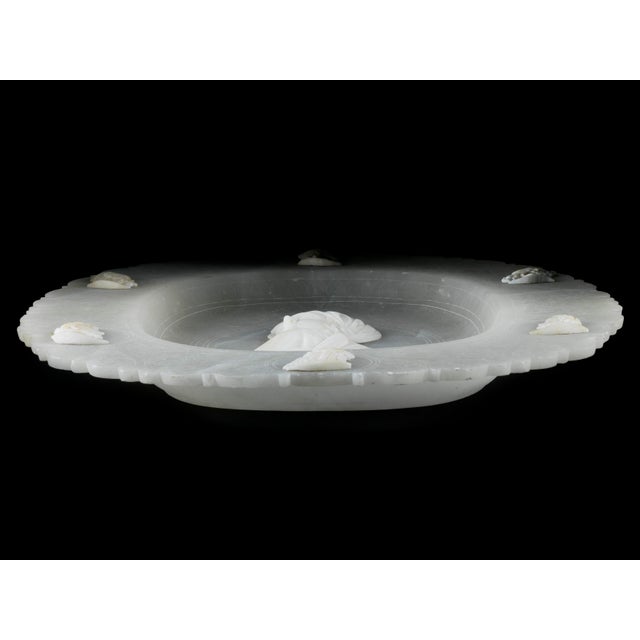 A translucent oval bowl made of alabaster with a lobed rim, ornamental engravings in the style of the Renaissance and...