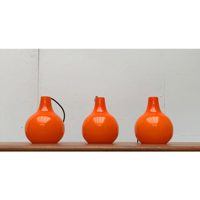 Mid Century glass pendants from the renowned manufacturer Putzler. The lamp body made of orange flashed glass shows an...