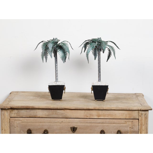 A pair of French vintage painted tôle palm tree sculptures from the mid 20th century, with tapered pot and lion ring...