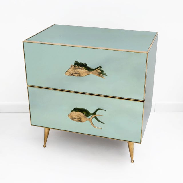 Elegant pair of nightstands featuring a refined structure clad in aqua green mirrored glass, enhanced by slender brass...