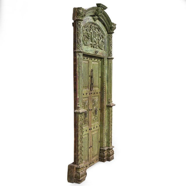 A very large antique carved wooden door, richly decorated with floral motifs, side columns, and a curved pediment with a...