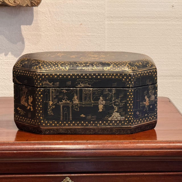 A lacquered box of canted rectangular form, decorated overall in gilt on a black ground with figures gathered among...