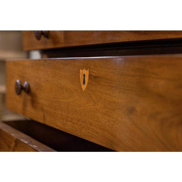 An Italian walnut commode from the 19th century with four drawers and inlaid shield-shaped ash escutcheons. Created in...