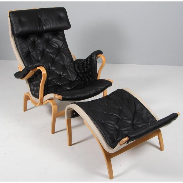 Bruno Mathsson Pernilla lounge chair with ottoman, original upholstery in black leather. Frame in lacquered beech. Made by...