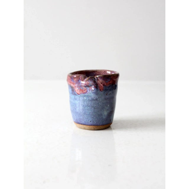 A vintage studio pottery vase, hand-crafted with a luminous blue glaze accented by a dramatic purple-pink drip along the...