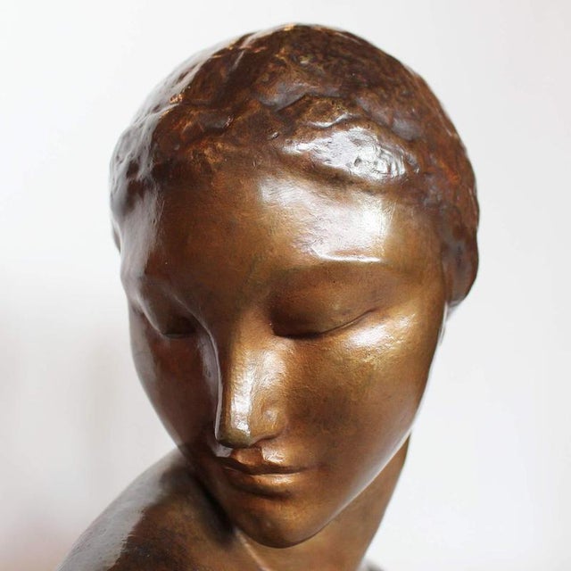 An art deco, patinated bronze bust of a young lady, head to one shoulder. Set over a freestanding wooden plinth. Signed a....