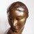 An art deco, patinated bronze bust of a young lady, head to one shoulder. Set over a freestanding wooden plinth. Signed a....