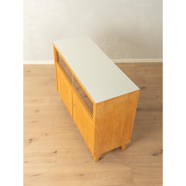 Classic chest of drawers from the 1950s. Ash veneer body with two sliding glass doors, two doors, one shelf, and angled...