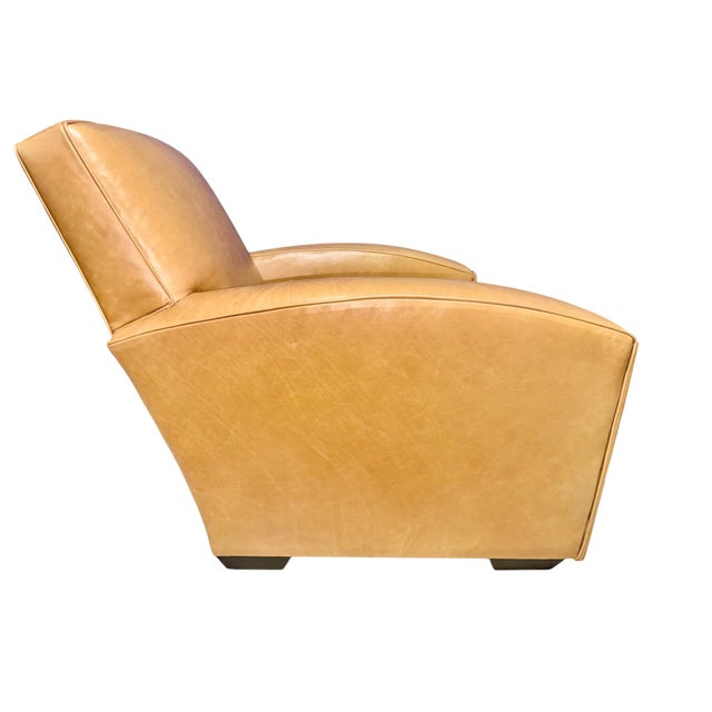 Classic club armchair upholstered in warm tan leather, featuring a deep, comfortable seat, softly sculpted arms, and a...