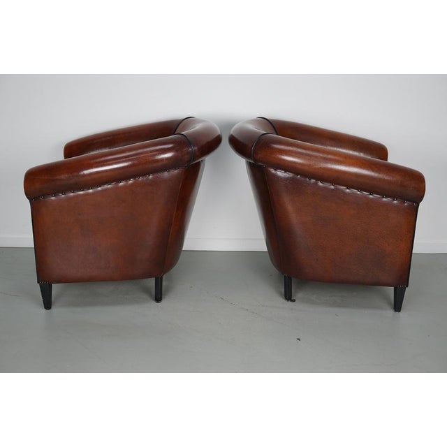 This pair of cognac-colored leather club chairs come from the Netherlands. They are upholstered with patinated cognac-...