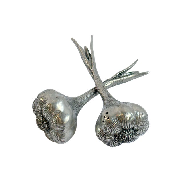 A whimsical pair of vintage silver-plated salt and pepper shakers modeled as crossed garlic bulbs with gracefully...