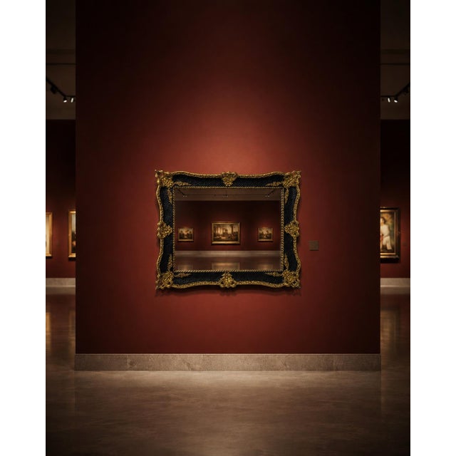 Ornate decorative wall mirror featuring a black frame with antique gold detailing and carved-style scrollwork. The piece...