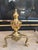 A decorative pair of vintage 1990s brass fireplace andirons in the Colonial Revival style. Each features a polished urn-...