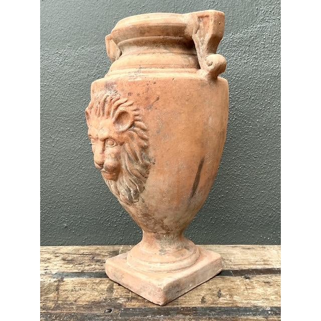 This striking terracotta urn is a masterclass in Classical Italianate design, featuring a prominent, high-relief lion’s...
