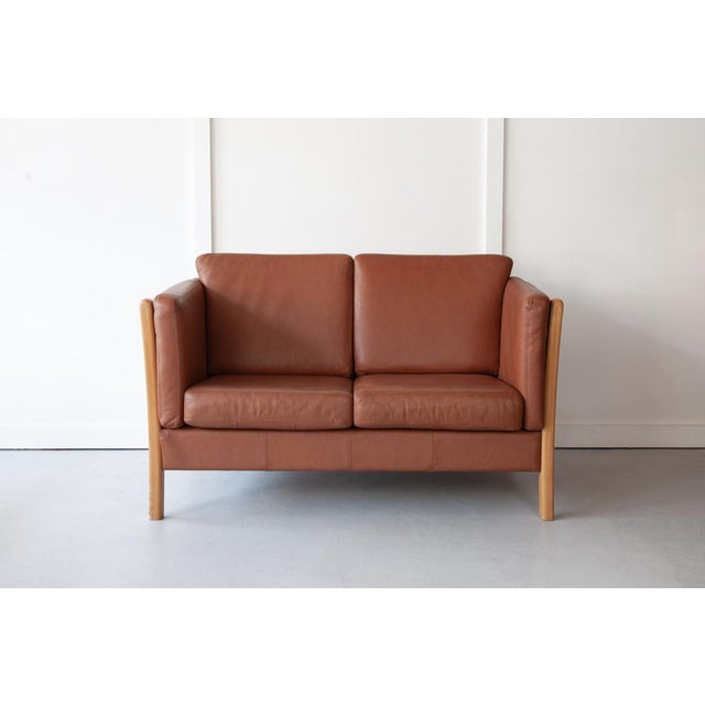 An elegant, brown leather two-seater sofa, manufactured by Mogens Hansen, Stouby with a pleasing beech frame and quality...
