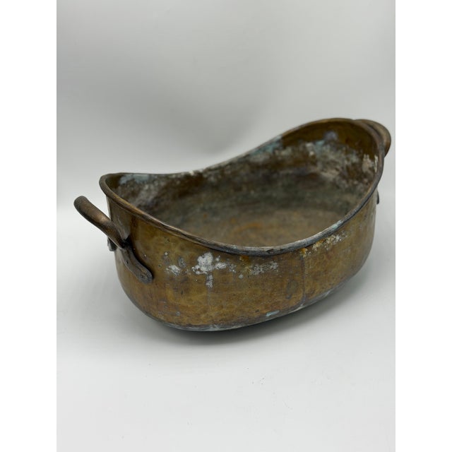 This is a wonderful antique hand-hammered brass vessel, with a low oval form, gently undulating rim, and substantial loop...