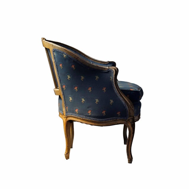 Antique, French Louis XV style armchair with a carved wood frame and blue floral upholstery.