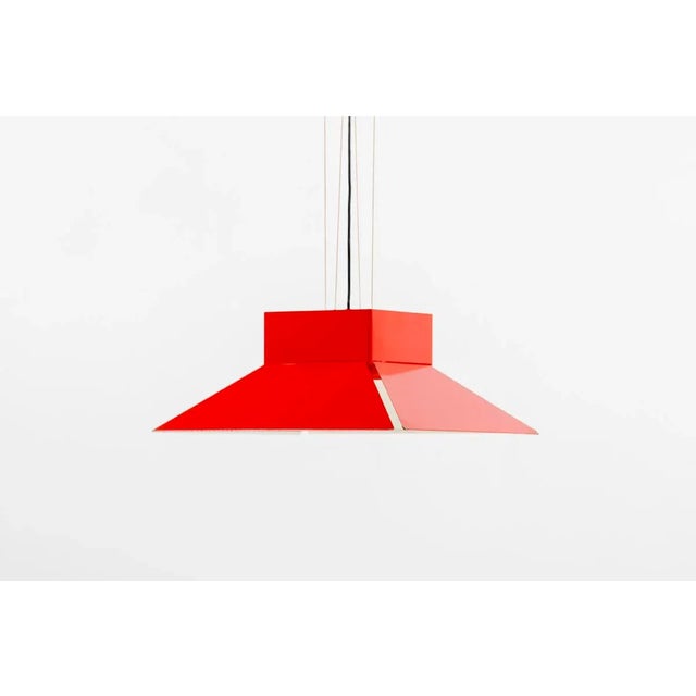 The lamp features a red enameled metal shade that hangs on four chords from a red ceiling fixture in the same material....