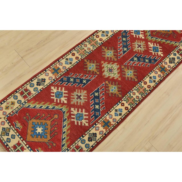 A tribal Caucasian Kazak runner hand-knotted with fine wool on a cotton foundation. This rug features geometric motifs set...