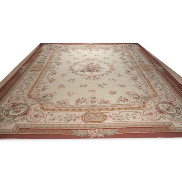 Vintage Aubusson in the Louis Philippe style. A wreath of pink roses tied with ribbons sits at the centre of a pale ivory...