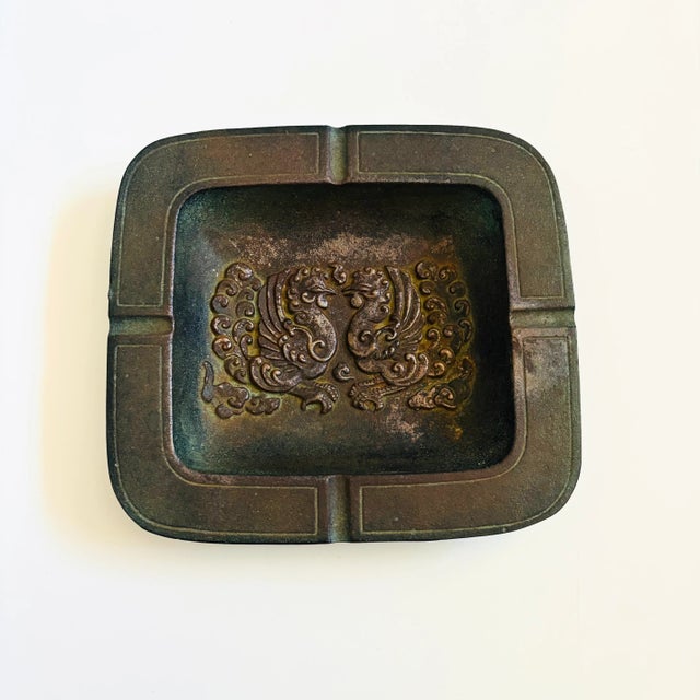 A vintage cast iron ashtray with an embossed design of 2 roosters in the center. Slight verdigris patina, more visible on...