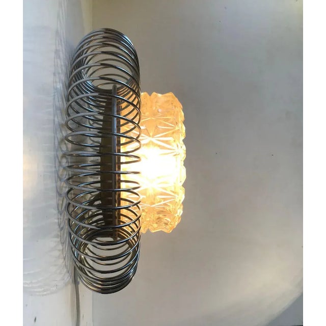Unusual wall sconce with chrome plated perimeter of spiral steel and centershade in pressed glass. It resembles a bursting...