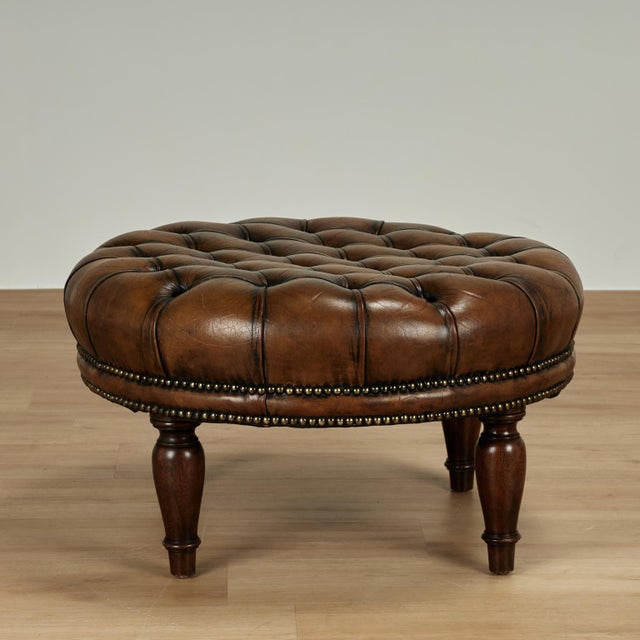 Handsome vintage ottoman upholstered in lush brown leather with button tufting, brass tacks and turned mahogany legs.