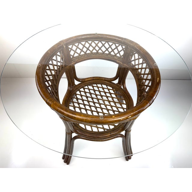 A refined vintage rattan side table crafted in the style of McGuire, featuring a round glass top over an elegantly...