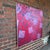 This abstract painting features a large red field covered with cylindrical shape, tumbling objects. The white blocks...