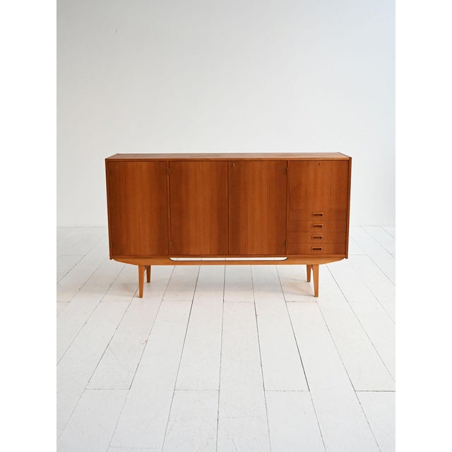 Northern European production, 1950s–1960s. Teak highboard with tapered legs, hinged doors, internal shelves, and a side...