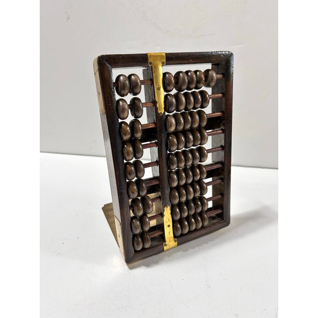 A sculptural vintage abacus bookend featuring a dark wood frame, sliding wooden beads, and handsome aged brass detailing....