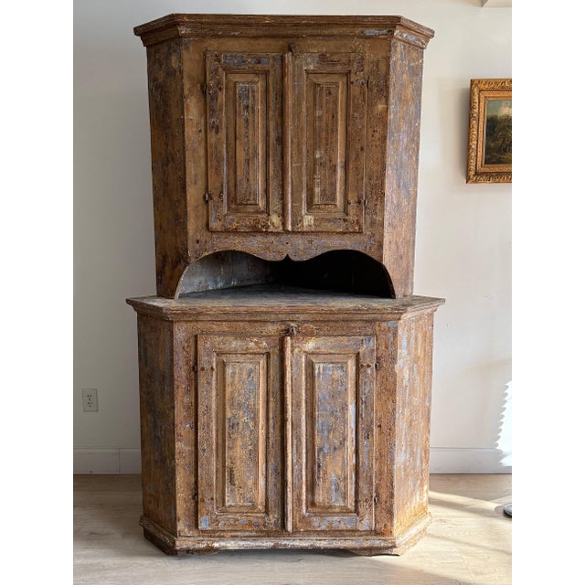 A tall 18th-century Swedish cupboard in dry scraped paint, the blue and ochre worn back to bare wood across the canted...