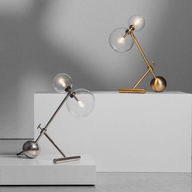 With a clear suggestive illumination, the Zosia table lamp elevates twin points of light upon thin rods, suspended within...