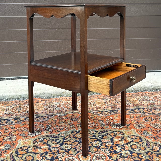 A vintage Saybolt Cleland English Traditional mahogany two tier nightstand having a shaped top apron over an open shelf...