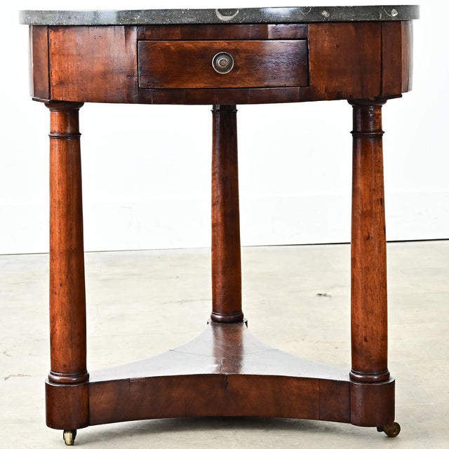 A 19th-century Empire-style gueridon with dark grey marble atop a mahogany base. The marble is punctuated with stunning...