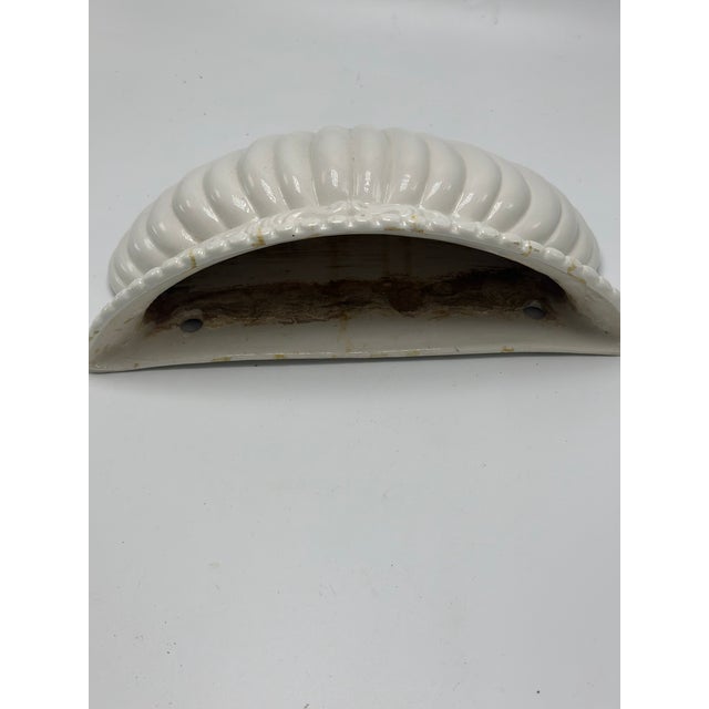 A charming vintage ceramic wall pocket modeled as a stylized scallop shell, featuring a crisp white glazed finish with...