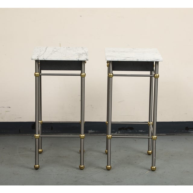 Pair of 20th Century Hollywood Regency Style marble, brass and steel end tables. The slim steel frame has a soft brushed...