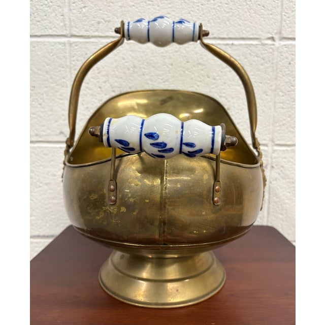 This is a vintage brass coal scuttle featuring ornate lion-head accents, porcelain delft roller handles, and a classic...