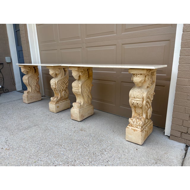 An extraordinary pair of neoclassical console tables featuring sculptural winged mythological figures supporting...