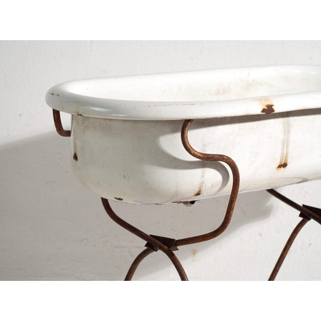 This antique bathtub in enamelled iron rests on a folding stand of bent iron tube. Originates from Central Europe, from...