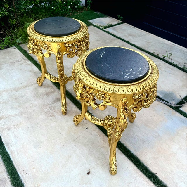 A sophisticated matching set of two French-style side tables, each featuring an ornate gold-leaf frame and a dramatic...