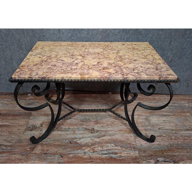 An elegant coffee table or side table, combining a wrought iron base with a marble top in natural hues. The rectangular...