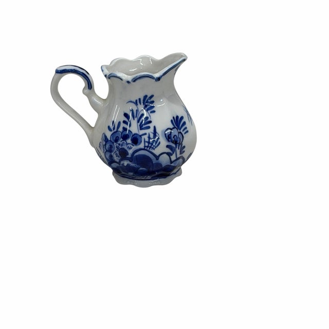 This piece is a Delft Blue creamer or miniature pitcher, which typically features a hand-painted scene of a Dutch windmill...