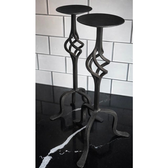 Pair of mid-century sculptural iron candlesticks in solid iron. Matching pair with elegant twisted stems and tripod bases....